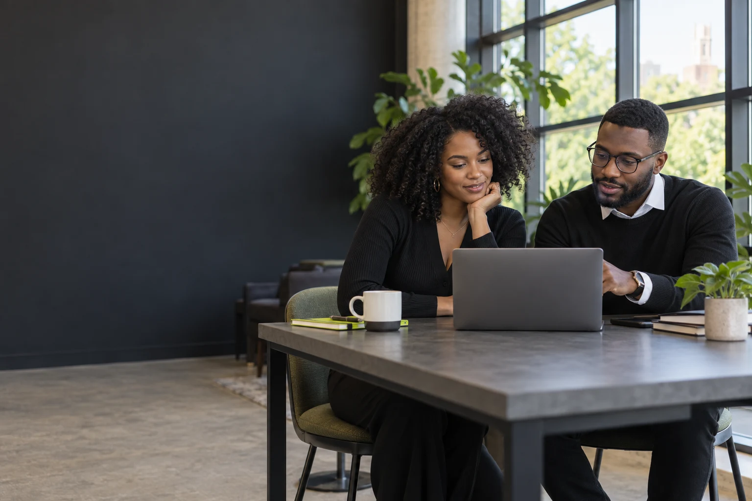 Two Black professionals working together on a laptop in a bright coworking space